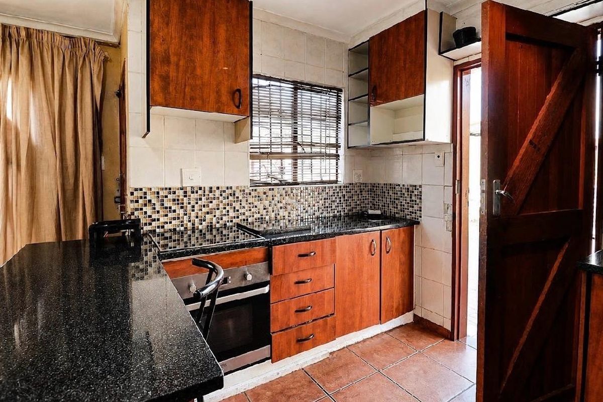 A functional kitchen featuring dark granite countertops, wood-finish cabinetry, built-in oven and hob, and tiled flooring with direct access to an exterior area.