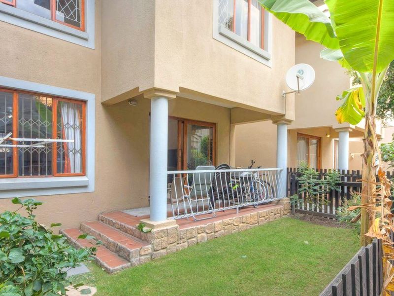 Rear view of the townhouse featuring a covered patio with stone-clad steps, metal balustrade, and a small private garden area with timber fencing.