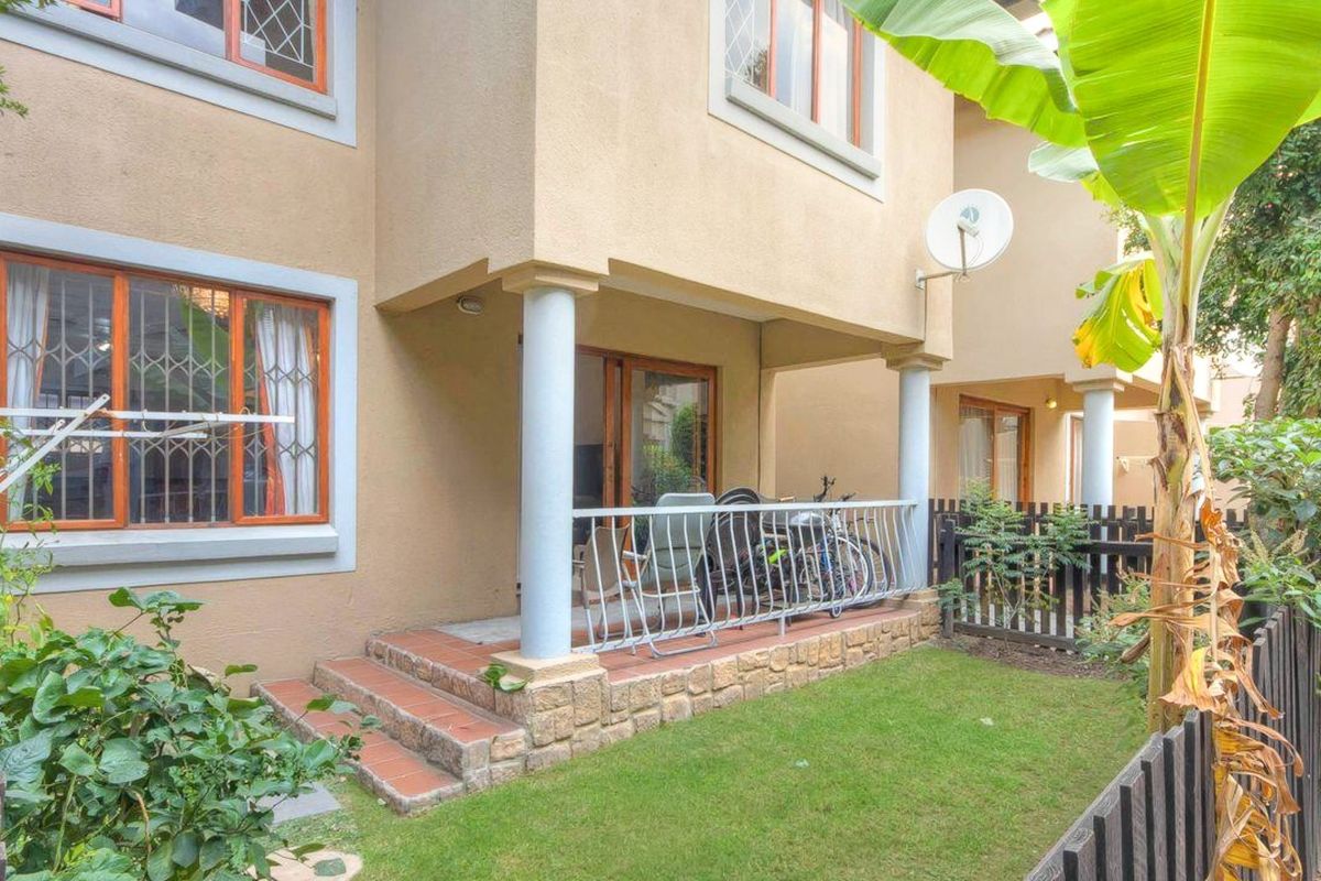 Rear view of the townhouse featuring a covered patio with stone-clad steps, metal balustrade, and a small private garden area with timber fencing.