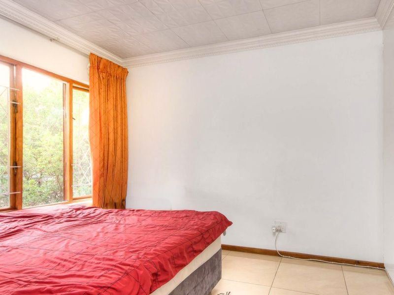 A bedroom featuring tiled flooring, a built-in wardrobe, and large timber-framed windows with security bars, offering a functional and well-lit living space.