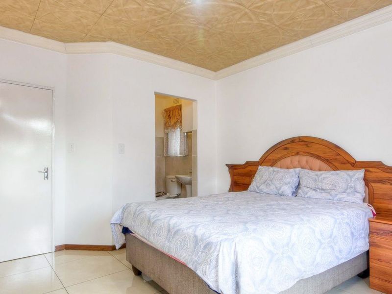 A bedroom featuring tiled flooring and a textured ceiling, with direct access to an adjoining en-suite bathroom.