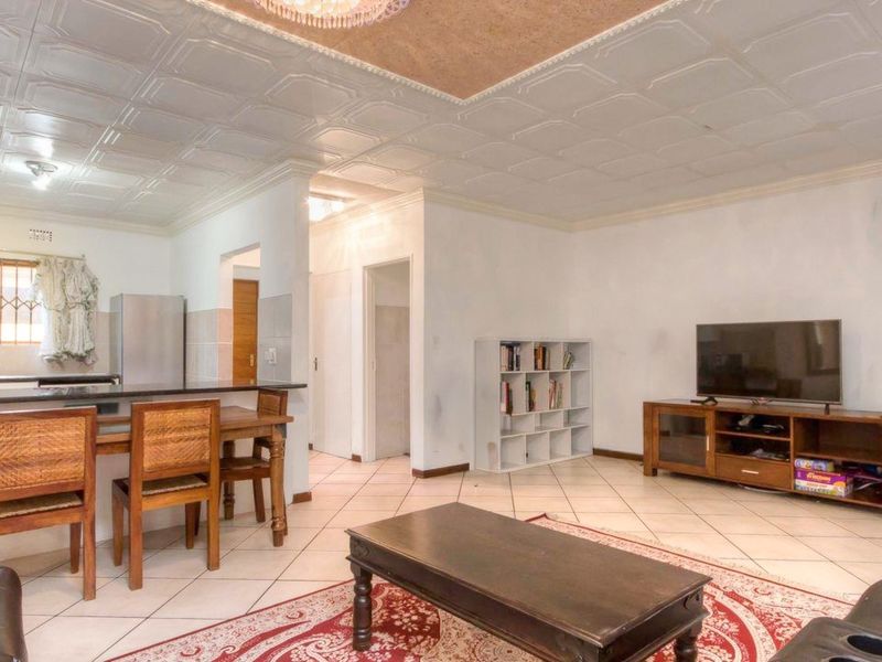 Open-plan living and kitchen area featuring tiled flooring, a breakfast counter, and decorative ceiling tiles, providing a functional and connected living space.