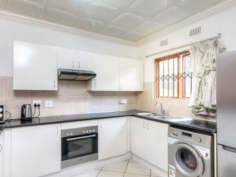 Functional kitchen featuring white cabinetry, granite countertops, built-in oven, hob, extractor fan, and tiled backsplash with a double sink and security window bars.