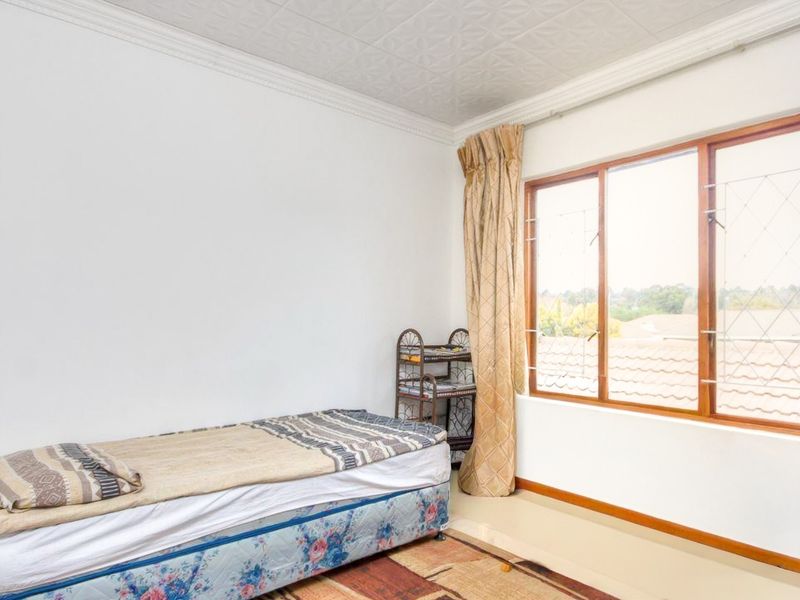 A bedroom featuring timber-framed windows with security bars and a textured ceiling, offering a functional space with natural light.