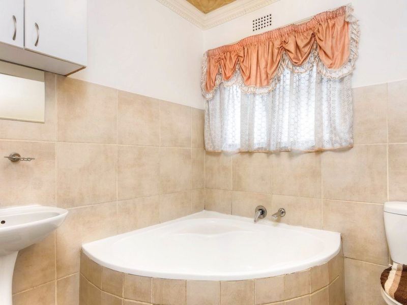 A functional bathroom featuring a corner bathtub, pedestal basin, and toilet with neutral wall tiling.