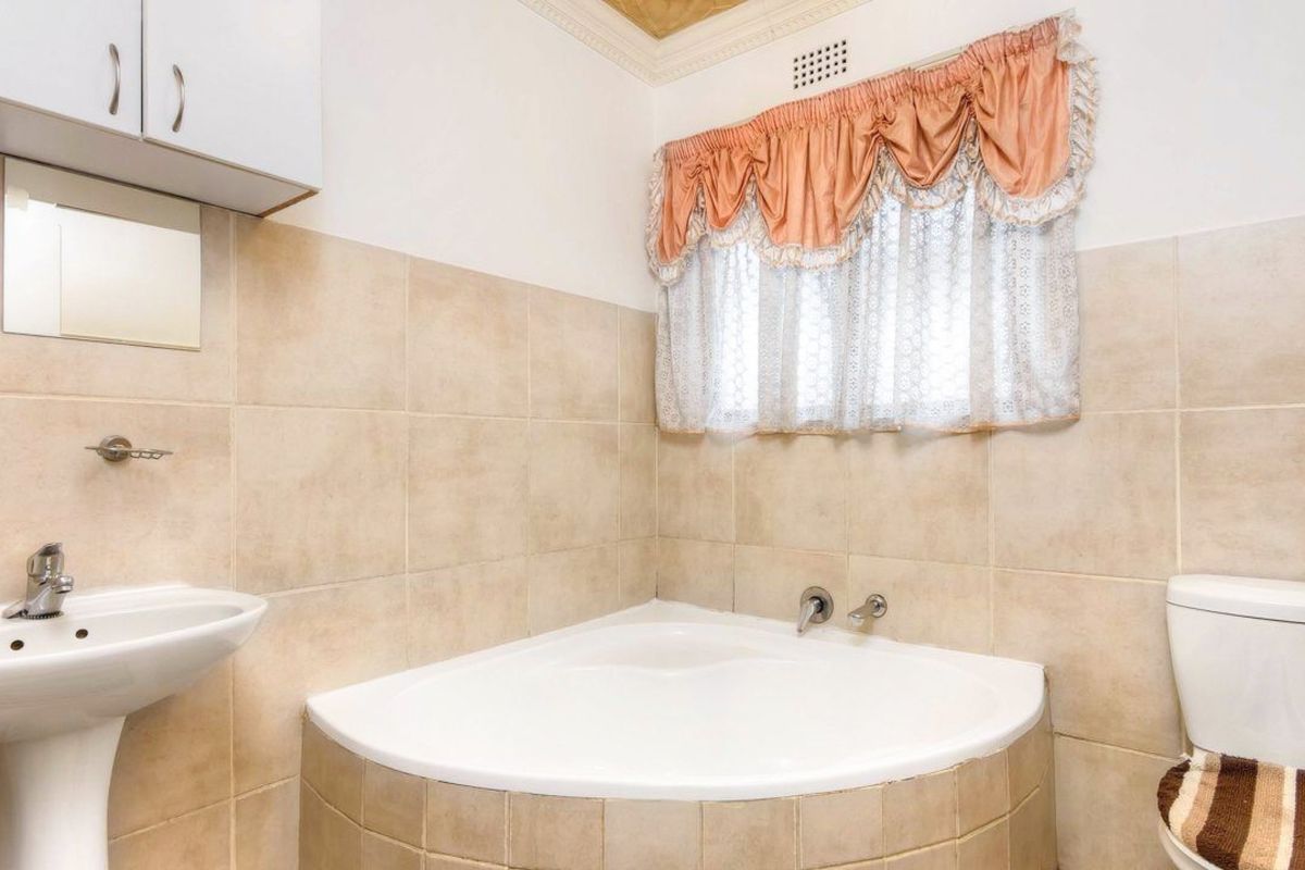 A functional bathroom featuring a corner bathtub, pedestal basin, and toilet with neutral wall tiling.