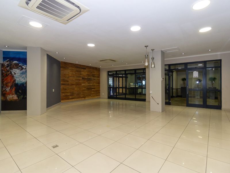 Spacious commercial entrance lobby featuring tiled flooring, recessed lighting, cassette air conditioning, and modern timber wall accents.