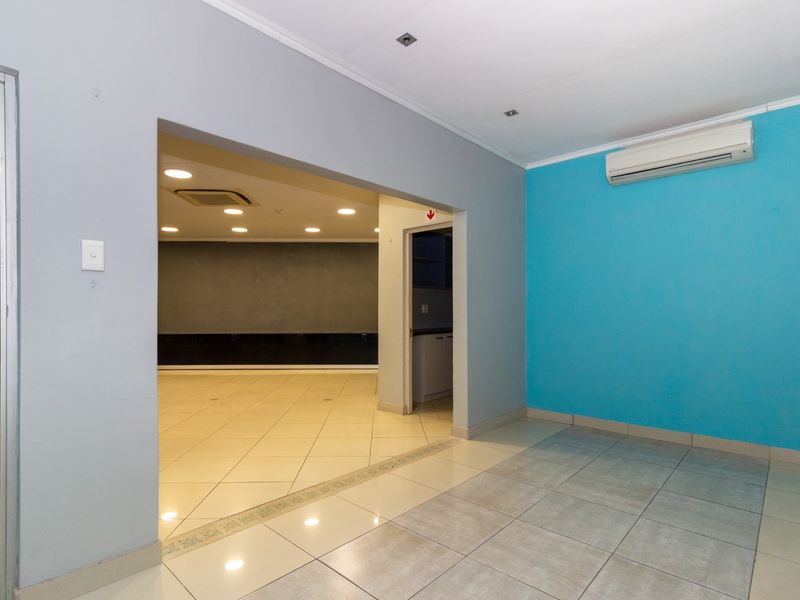 Spacious open-plan retail area featuring neutral and accent wall finishes, recessed lighting, tiled flooring, and a wall-mounted air conditioning unit.