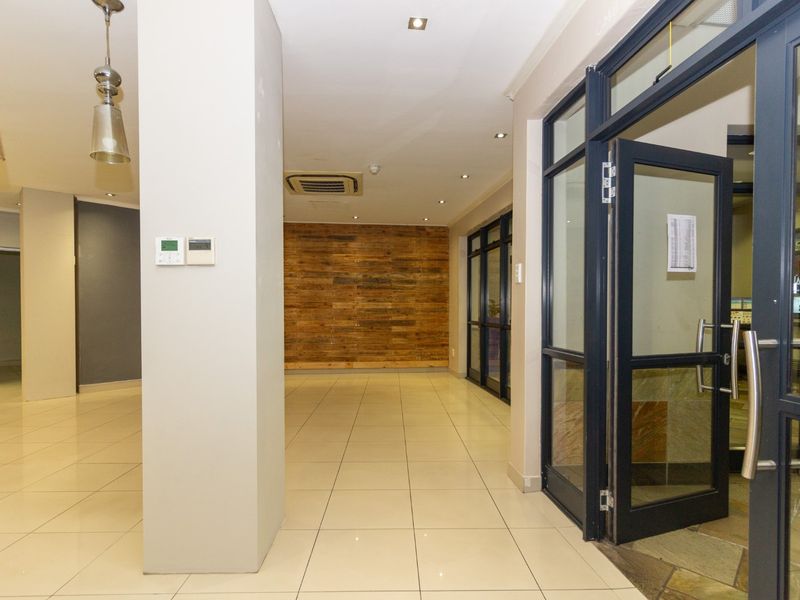 A bright and modern commercial entrance area featuring tiled flooring, timber accent wall cladding, recessed lighting, and a glass-panelled aluminium door.
