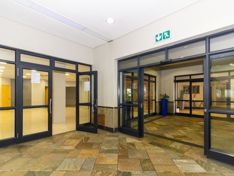 A bright and professional commercial entrance lobby featuring natural stone flooring, aluminium-framed glass doors, and recessed lighting, providing a clean and welcoming access point.
