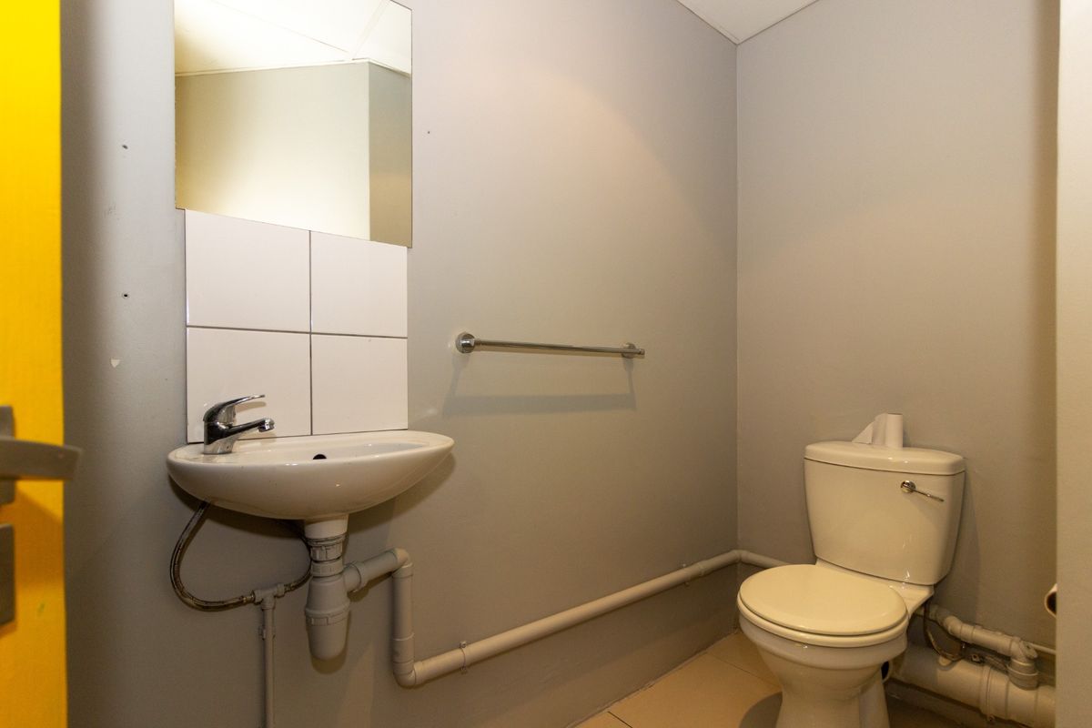 A compact functional bathroom featuring a wall-mounted basin with tiled splashback, toilet, and exposed surface-mounted plumbing.