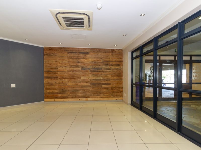 A bright, modern commercial entrance area featuring tiled flooring, a timber accent wall, and large glass doors providing natural light and street visibility.