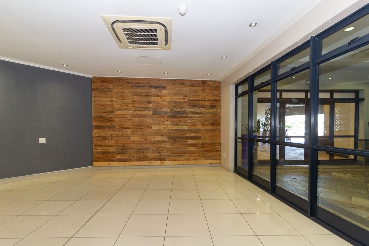 A bright, modern commercial entrance area featuring tiled flooring, a timber accent wall, and large glass doors providing natural light and street visibility.