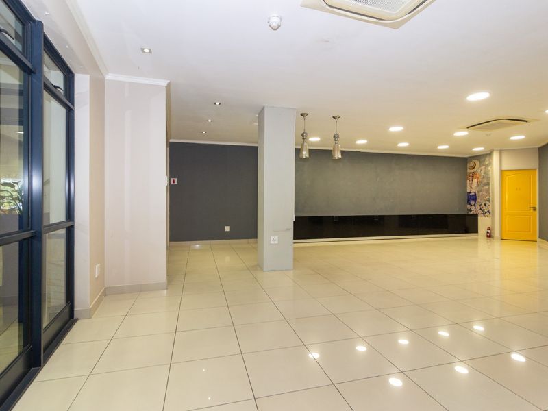Spacious open-plan retail area featuring polished tile flooring, recessed lighting, a central support column, and built-in low-level cabinetry.