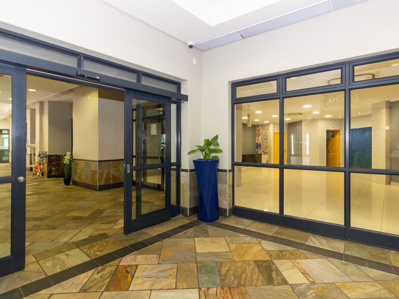 A bright and modern retail entrance featuring stone tile flooring, large aluminum-framed glass doors, and recessed ceiling lighting.