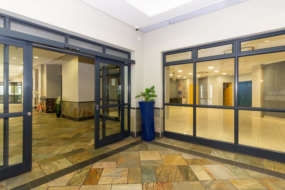 A bright and modern retail entrance featuring stone tile flooring, large aluminum-framed glass doors, and recessed ceiling lighting.