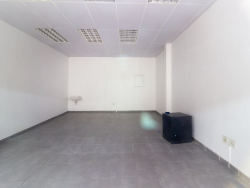 An empty, functional retail utility space featuring tiled flooring, a suspended ceiling with recessed lighting, and a wall-mounted basin.