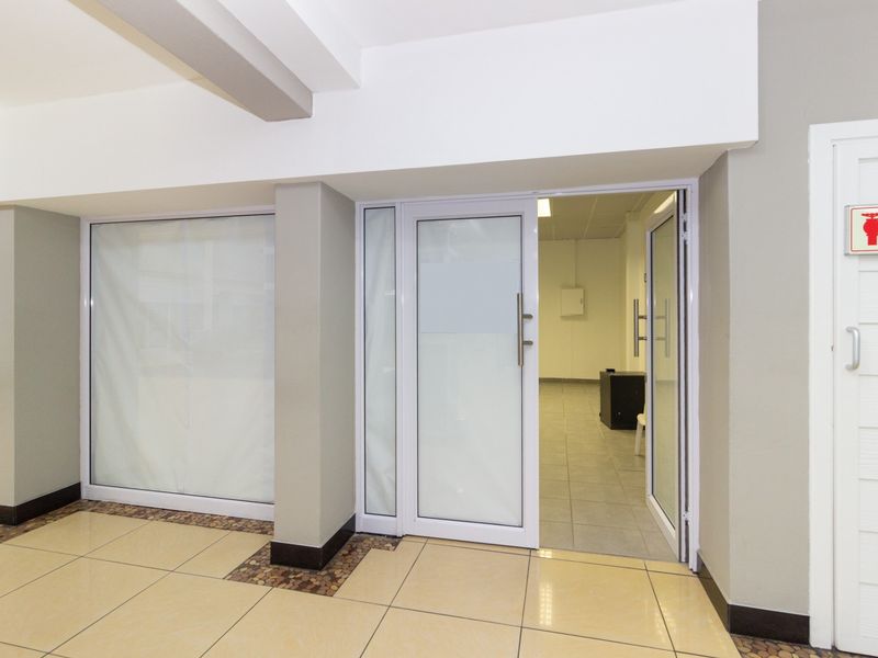 A clean, modern retail entrance featuring tiled flooring, white aluminium-framed glass doors, and clear fire safety signage.