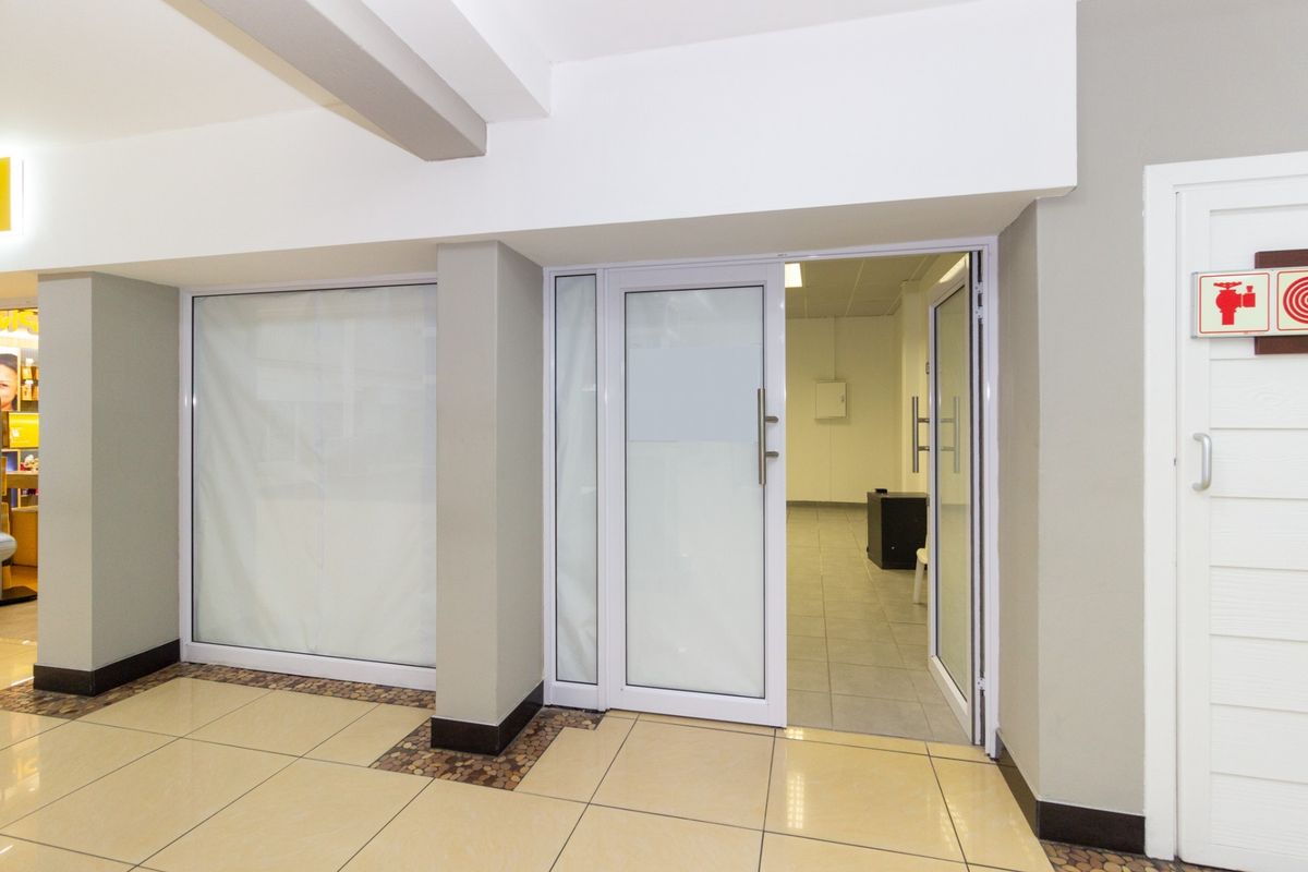 A clean, modern retail entrance featuring tiled flooring, white aluminium-framed glass doors, and clear fire safety signage.