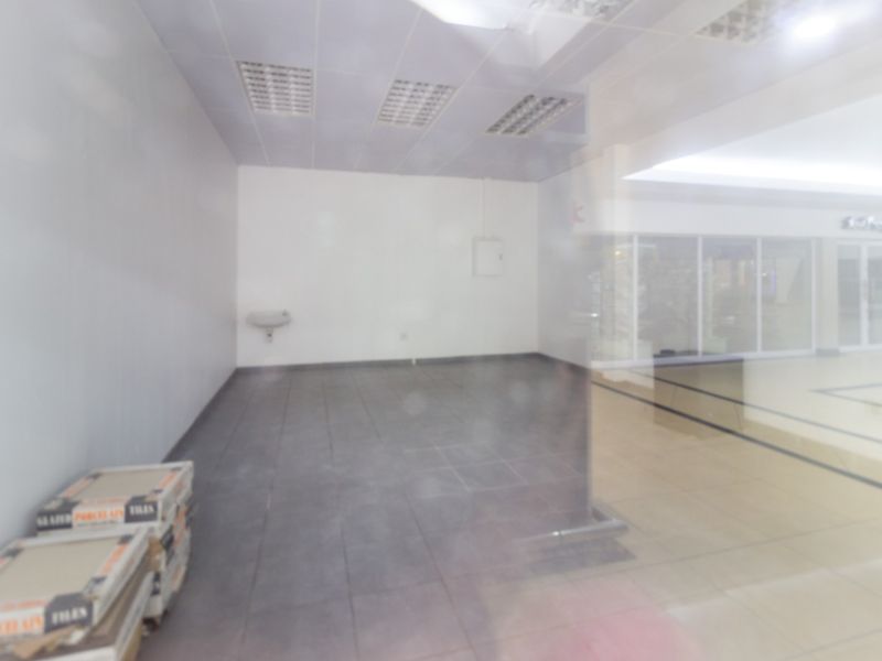 An empty retail utility space featuring tiled flooring, a suspended ceiling with recessed lighting, and a wall-mounted basin.