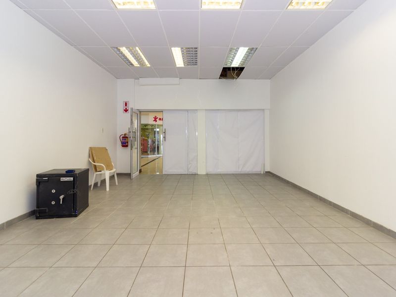 An open-plan retail space featuring ceramic tiled flooring, a suspended ceiling with recessed lighting, and a glass entrance door.