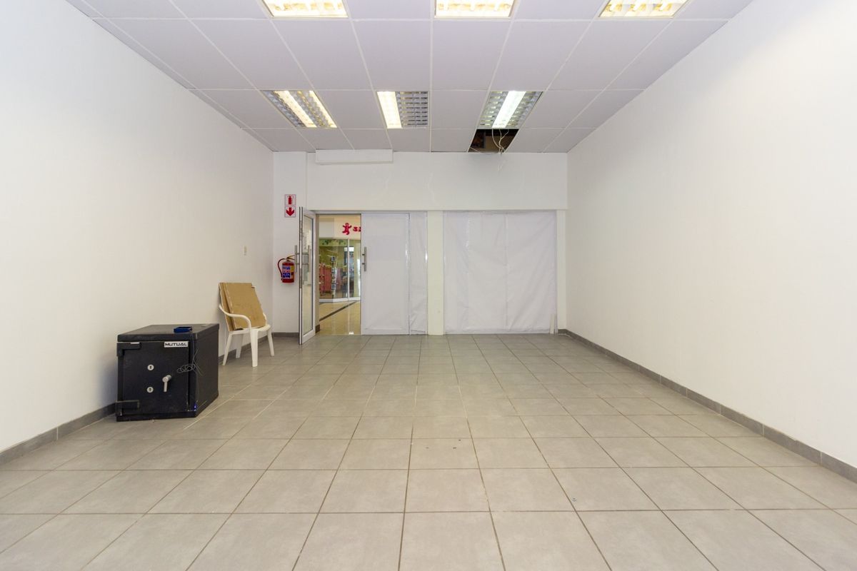 An open-plan retail space featuring ceramic tiled flooring, a suspended ceiling with recessed lighting, and a glass entrance door.