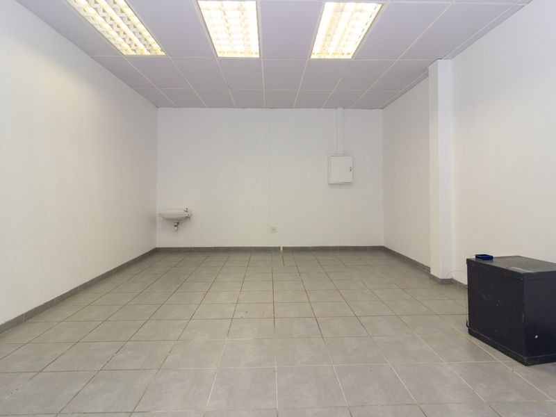A clean, vacant utility or storage space featuring ceramic tiled flooring, a wall-mounted basin, and functional suspended ceiling lighting.