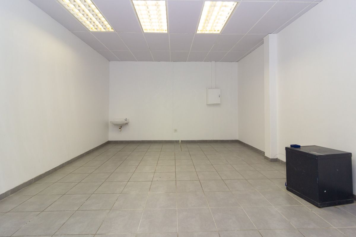 A clean, vacant utility or storage space featuring ceramic tiled flooring, a wall-mounted basin, and functional suspended ceiling lighting.