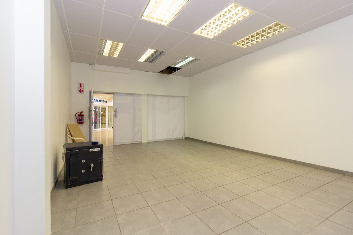 An empty open-plan retail space featuring ceramic floor tiles, a suspended ceiling with recessed lighting, and a fire safety installation.