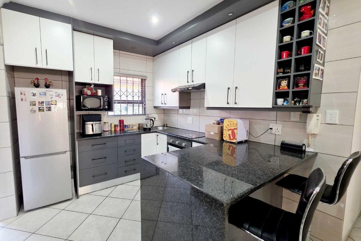 Modern kitchen featuring granite countertops, two-tone cabinetry, a breakfast bar, built-in oven, and tiled flooring with ample storage space.