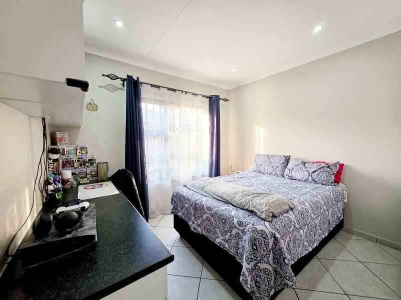 A well-lit bedroom featuring tiled flooring, recessed ceiling lighting, and a functional built-in desk area with a window fitted with security bars.