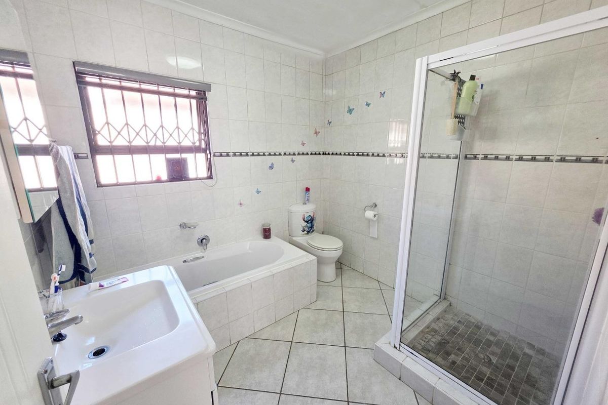 A functional bathroom featuring a built-in bathtub, separate shower enclosure, vanity basin, and toilet with tiled finishes throughout.