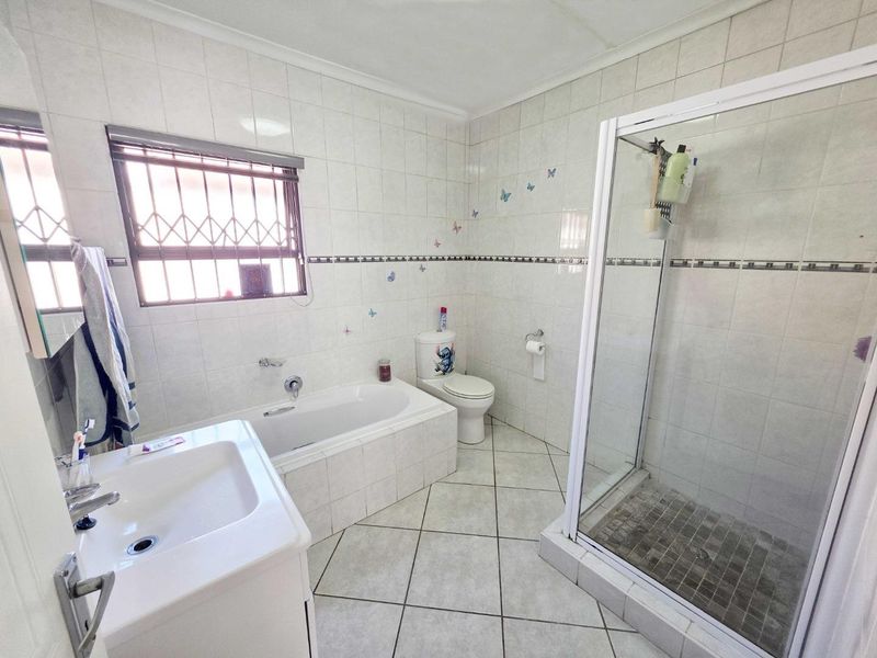 A functional bathroom featuring a built-in bathtub, separate shower enclosure, vanity basin, and toilet with tiled finishes throughout.