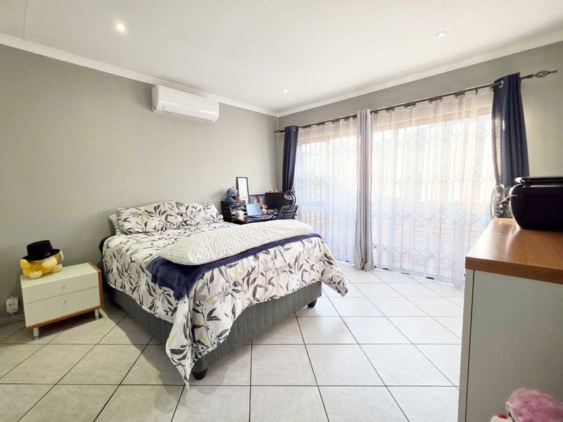 Spacious bedroom featuring tiled flooring, an integrated air conditioning unit, and large sliding glass doors with security gates providing access to the exterior.