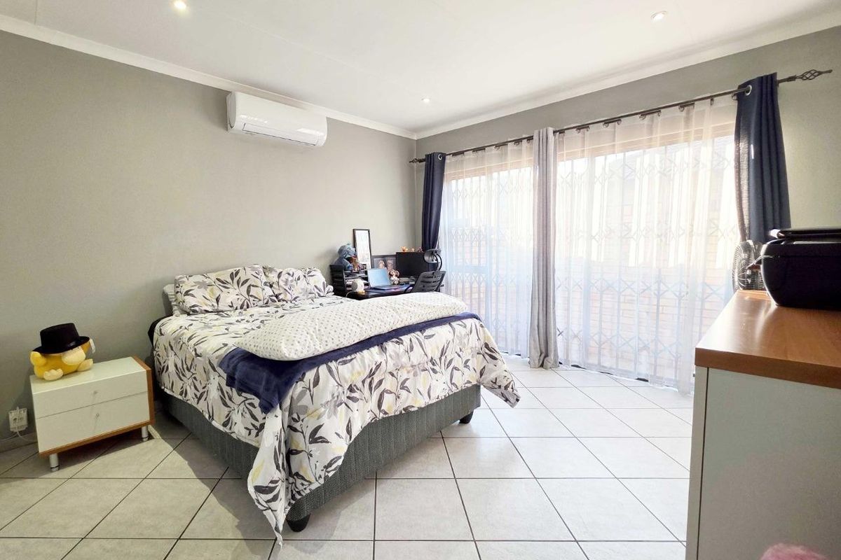 Spacious bedroom featuring tiled flooring, an integrated air conditioning unit, and large sliding glass doors with security gates providing access to the exterior.