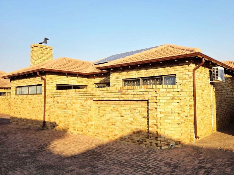 A well-maintained face brick townhouse exterior featuring a tiled roof, solar panels, and a paved driveway area.