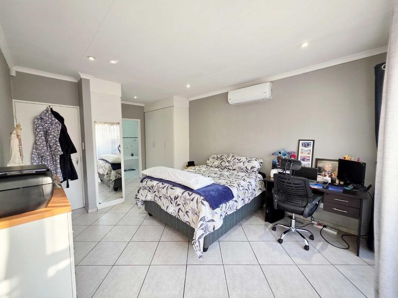 Spacious bedroom featuring tiled flooring, built-in cupboards, recessed lighting, and a wall-mounted air conditioning unit, with direct access to an en-suite bathroom.