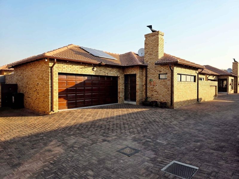 Front exterior view of a face brick townhouse featuring a double garage, tiled roof, solar panels, and a paved driveway.