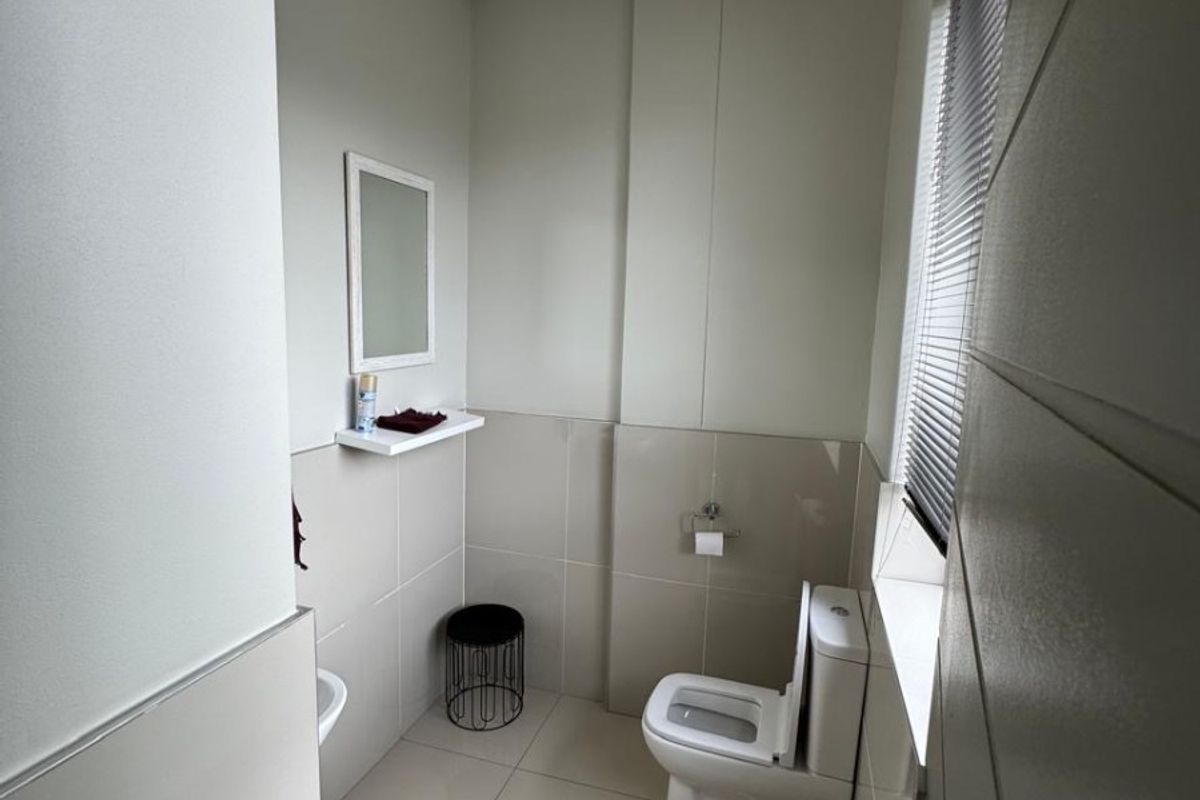 A clean, functional office bathroom featuring neutral tiled walls and flooring, a modern toilet, and a drop ceiling with integrated lighting.