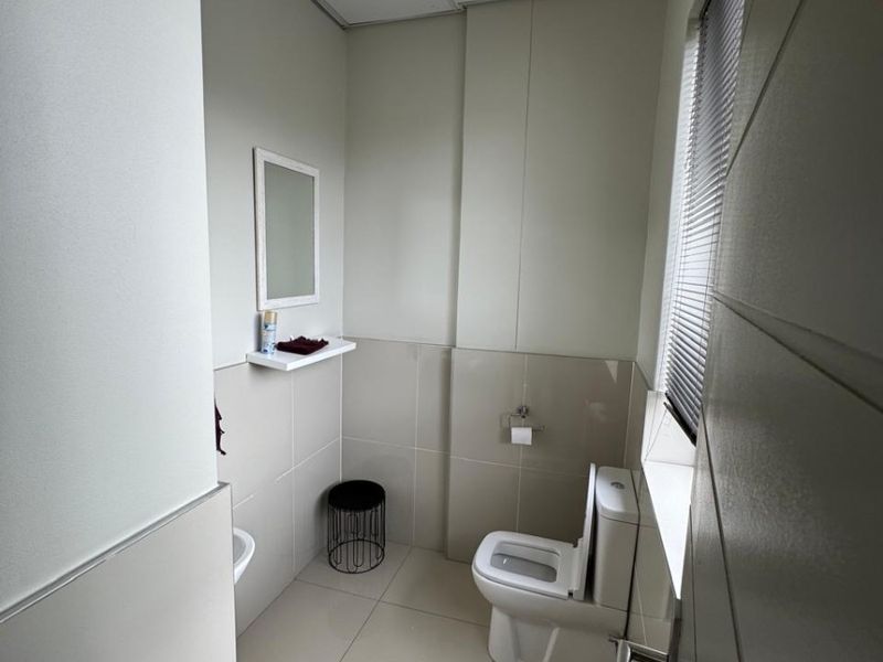 A clean, functional office bathroom featuring neutral tiled walls and flooring, a modern toilet, and a drop ceiling with integrated lighting.
