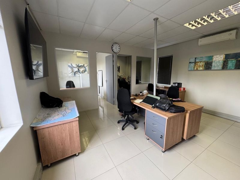 A functional office space featuring tiled flooring, a suspended ceiling with recessed lighting, internal glass partitions, and a wall-mounted air conditioning unit.
