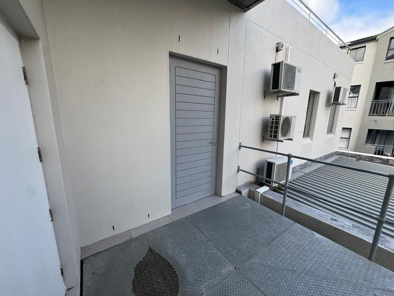 An exterior balcony area featuring metal flooring, safety railings, and wall-mounted air conditioning units.