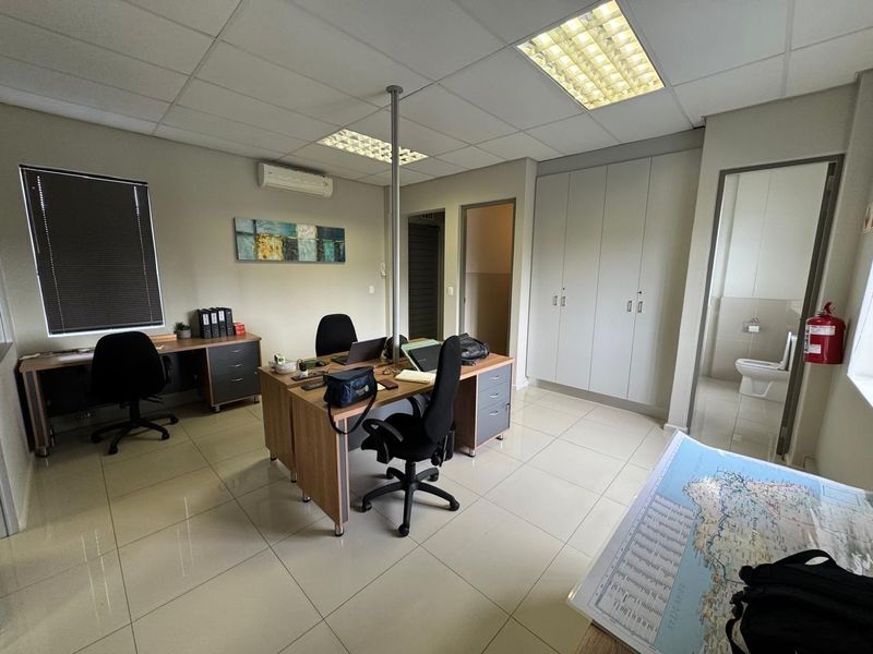 A functional office space featuring tiled flooring, suspended ceilings with recessed lighting, built-in storage cupboards, and an integrated split-system air conditioning unit.
