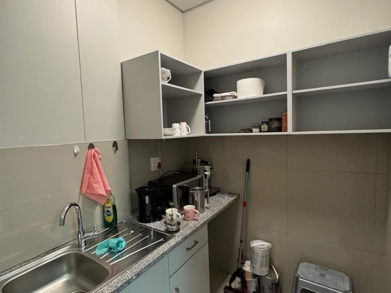 A functional office scullery area featuring built-in cabinetry, granite countertops, a stainless steel sink, and open shelving for storage.