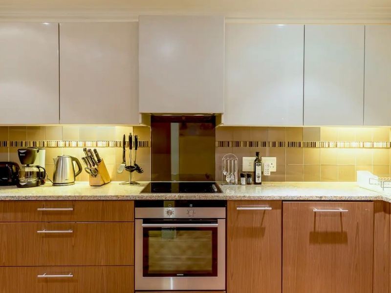 Modern kitchen featuring sleek two-tone cabinetry, granite countertops, a built-in oven with electric hob, and integrated extractor fan with under-cabinet lighting.