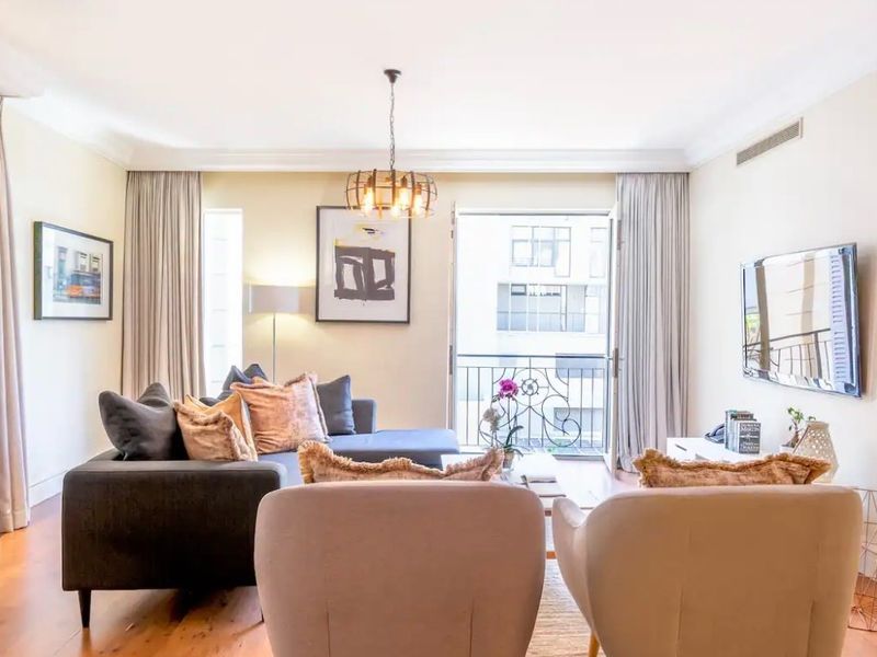 A well-maintained living room featuring hardwood flooring, decorative cove cornicing, and direct access to a private balcony through a glass door.
