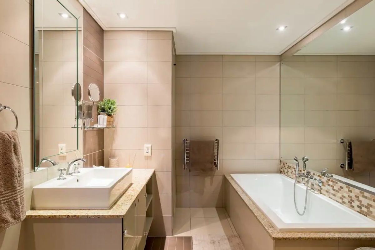 Modern bathroom featuring a vessel sink on a granite vanity, a built-in bathtub with mosaic tile accents, and neutral wall tiling.