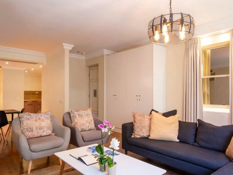 Spacious open-plan living area featuring hardwood flooring, crown molding, built-in cabinetry, and a modern pendant light fixture.
