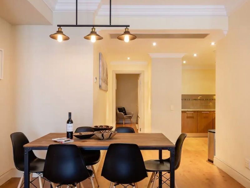 Open plan dining area featuring timber flooring, crown molding, and pendant lighting, with a view through to the kitchen and hallway.