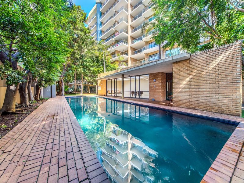 A well-maintained swimming pool area featuring brick paving, face brick walls, and direct access to the apartment building via large sliding glass doors.